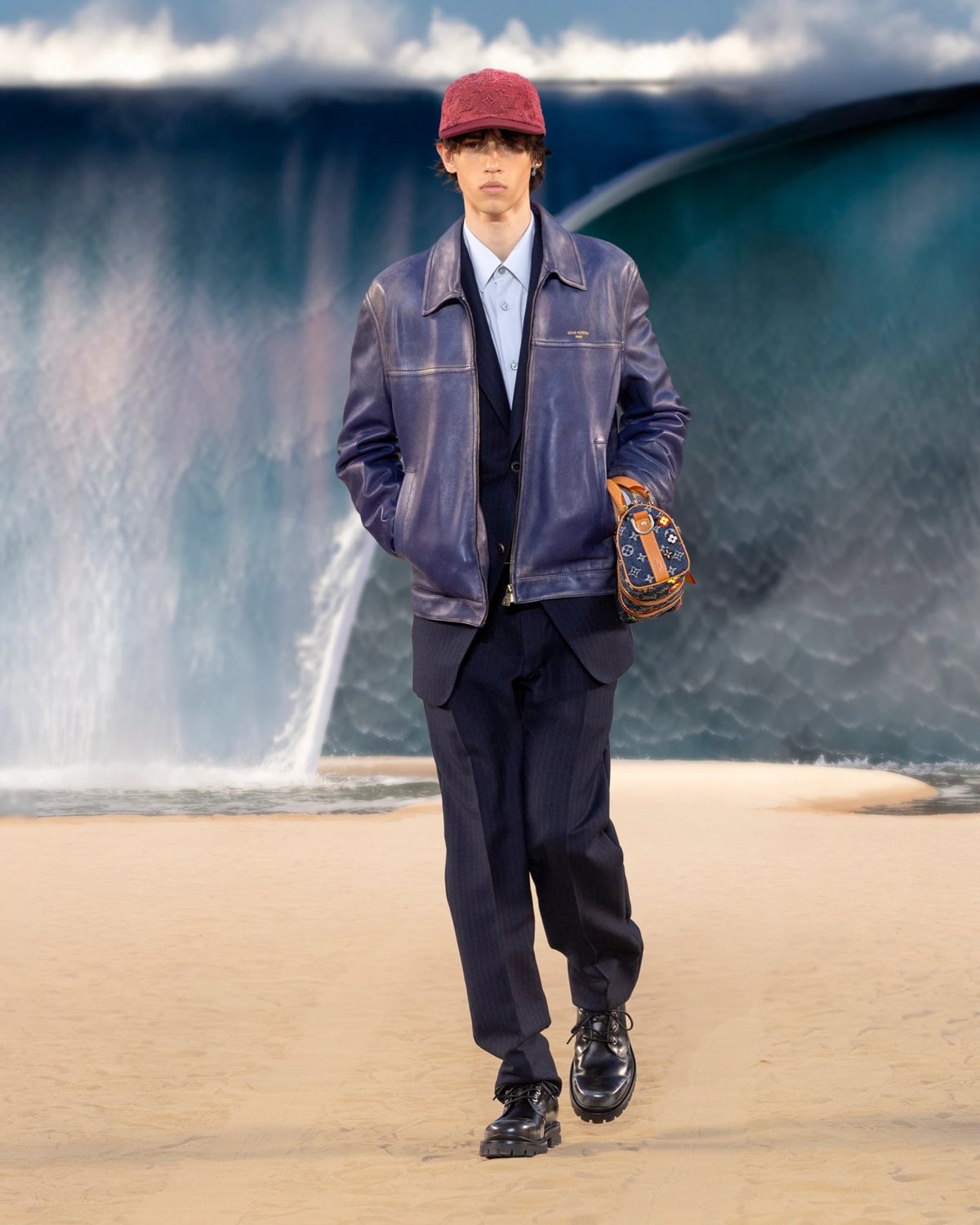 Look 014: แจ็กเก็ตสีน้ำเงินเข้มผิวเงาที่มีตัวอักษร Louis Vuitton Paris ซ้อนสูทกรมท่าลายริ้ว เชิ้ตสีฟ้า แคปสีเบอร์กันดีปักโมโนแกรม รองเท้าสีดำพื้นหนา และกระเป๋าใบเล็กโมโนแกรมสีน้ำเงินที่มีดอกไม้หลากสี การซ้อนหลายชั้นแบบนี้ไม่เหมาะกับไทยทั้งเซ็ต ยืมได้แค่หมวกกับกระเป๋า
